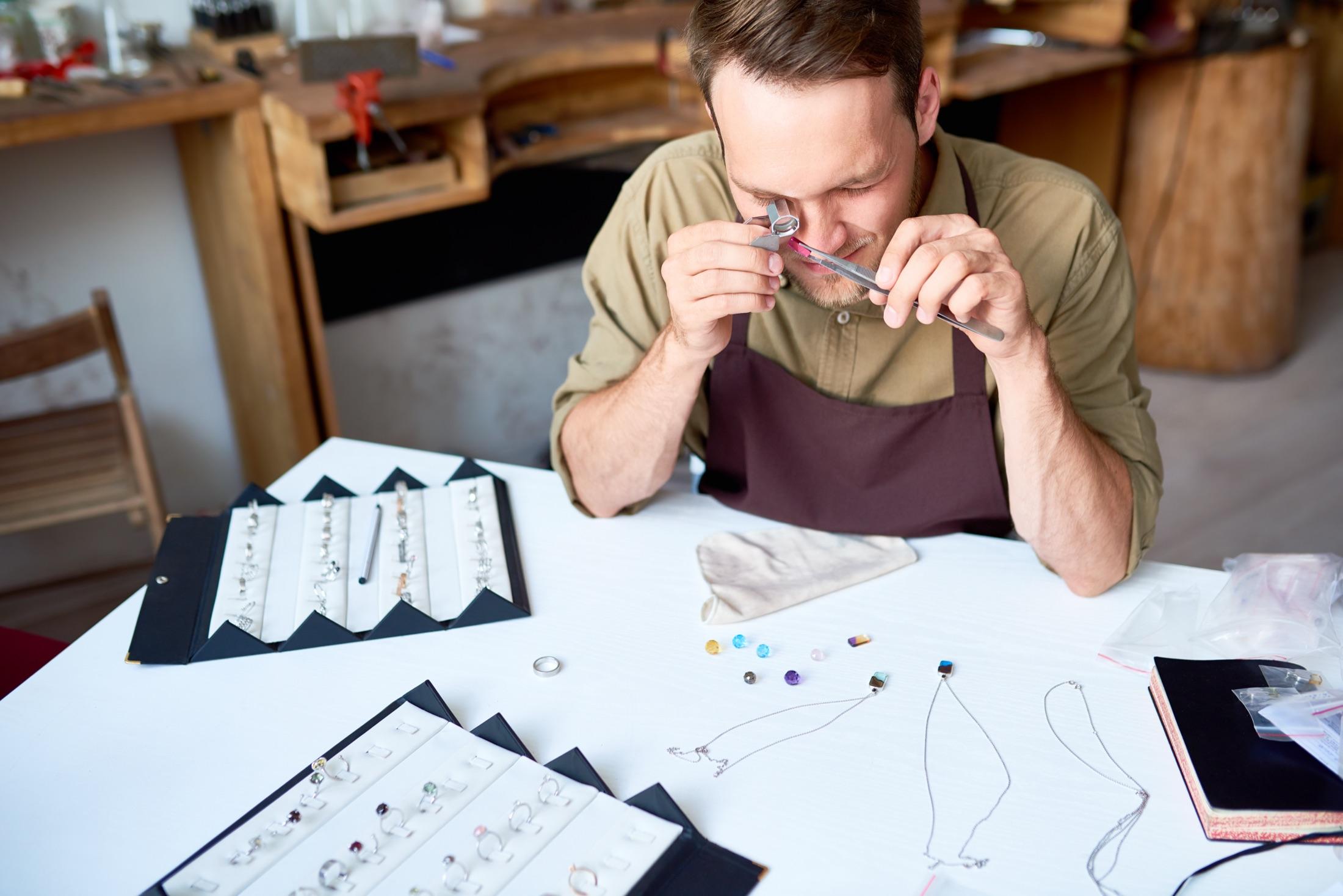 Jeweler examining a stone through a loupe, surrounded by gemstones and rings